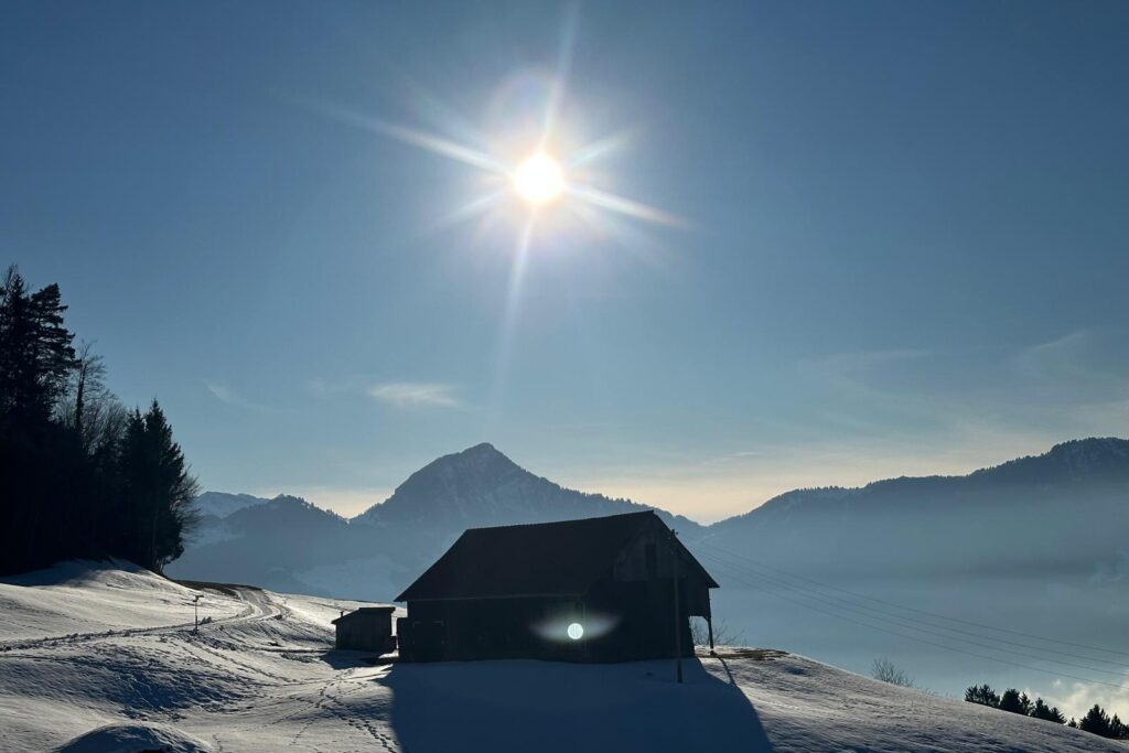 Schneelandschaft mit Sonne, blauem Himmel und einer kleinen Hütte – Symbol für Ruhe, Klarheit und innere Stille.